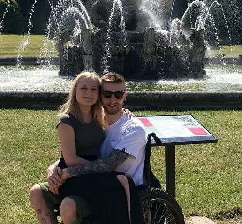 Becky sitting on Dan's lap in his wheelchair in front of a fountain