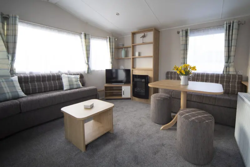 Accessible caravan lounge with sofa, coffee table, TV, electric fireplace and dining table