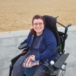 Emma sat by sandy beach in er wheelchair