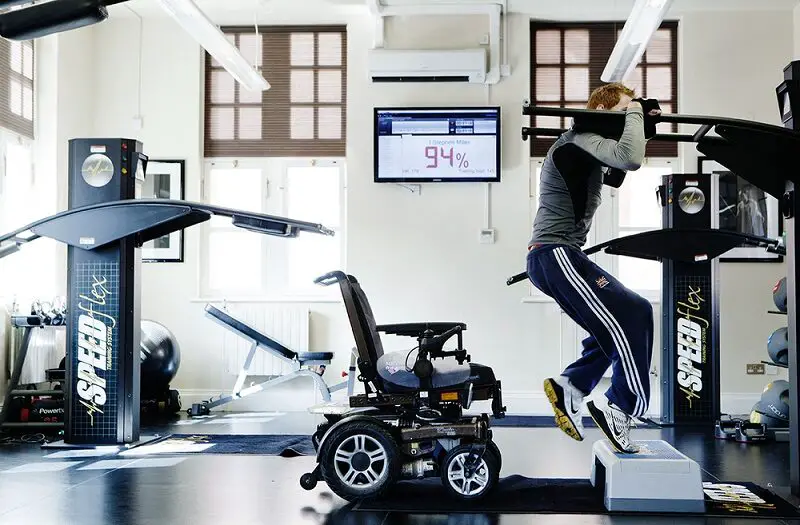 Paralympian Stephen Miller in a gym on an exercise machine with wheelchair behind him