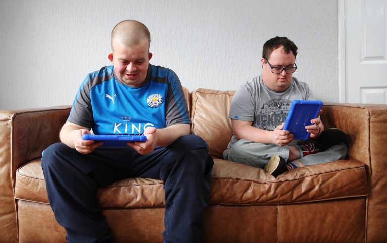 Two men with Down’s Syndrome using the Vodafone and Mencap MyLife app on their tablets sat on a sofa