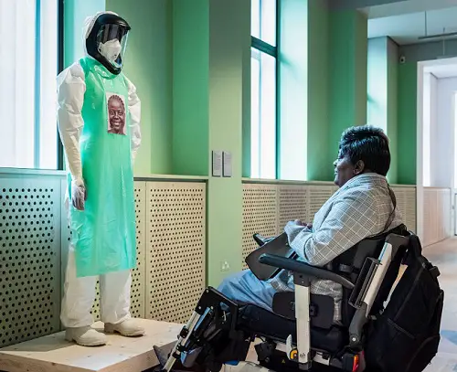 Woman in a wheelchair looking at a dummy in a medical uniform