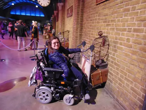 Emma in her wheelchair holding the luggage carrier going through a brick wall