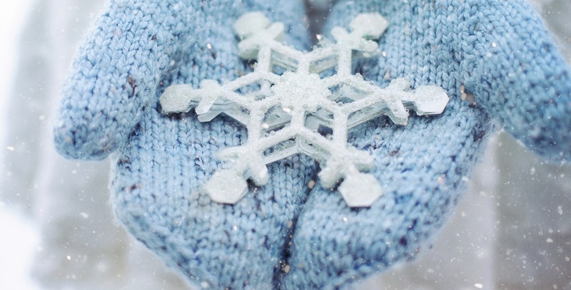 Hands wearing blue woollen mittens holding a snowflake