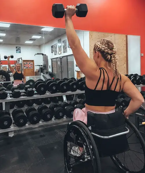 Sophie Carrigill in her wheelchair lifting a weight in front of a mirror in a gym
