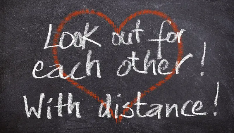 Words 'look out for each other with distance' in chalk on a blackboard