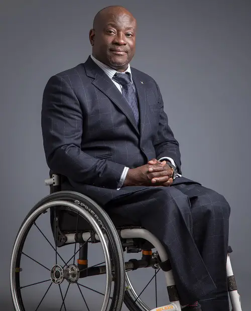 Mark Esho in a suit and his wheelchair on a grey background