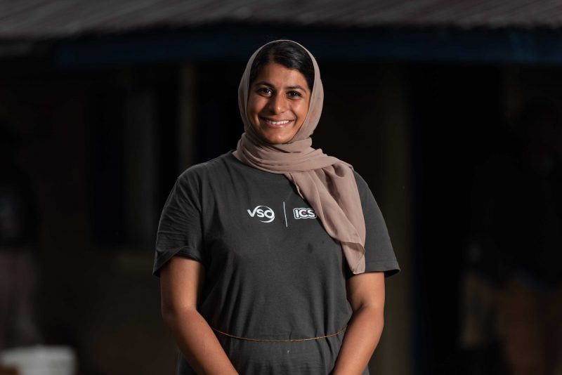 Raaiba stands smiling wearing a hijab and her VSO volunteer shirt