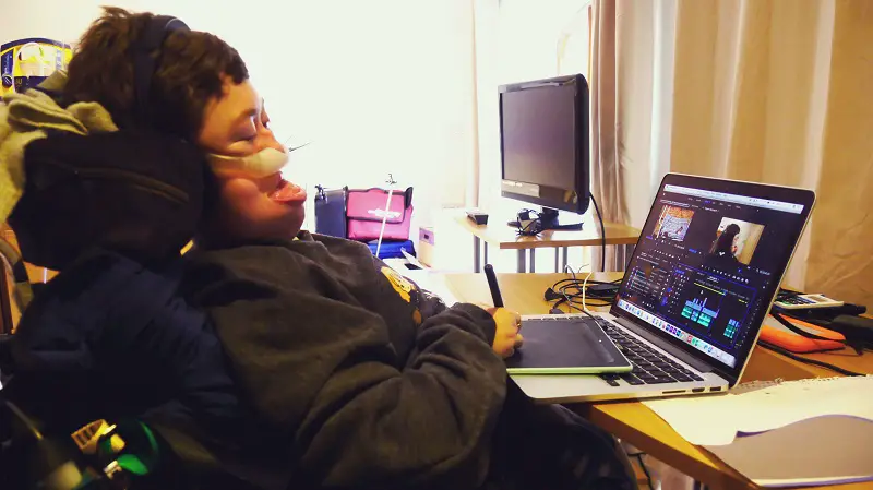 Stephanie Castelete-Tyrrell in her wheelchair at her laptop on a desk editing a film