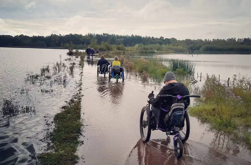 Group of disabled people in all-terrain wheelchairs going through a wet and boggy path