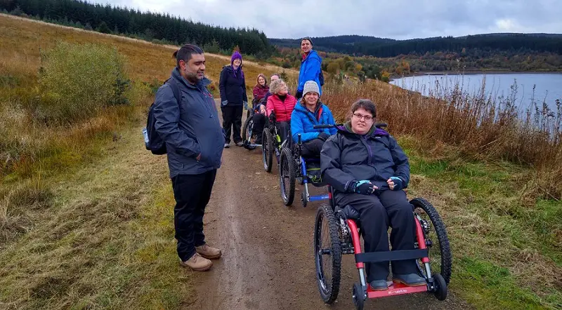 Group of disabled people in all-terrain wheelchairs on a ramble next to a lake