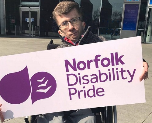 Man in a wheelchair holding the Norfolk Disability Pride sign