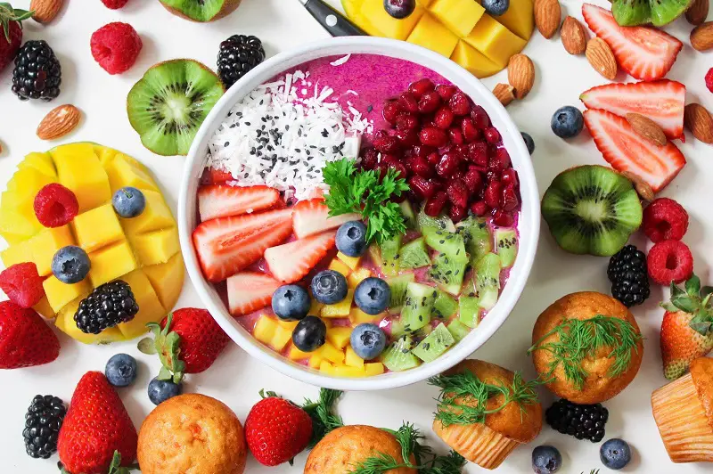Mix of fruit in a bowl with yoghurt surrounded by fruit and muffins
