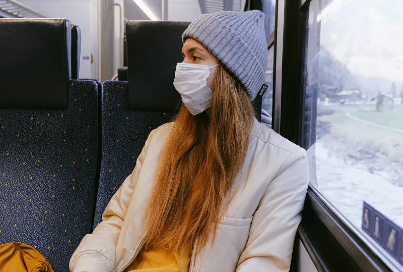 Woman on a train wearing a face mask wearing a grey knitted hat and cream coat