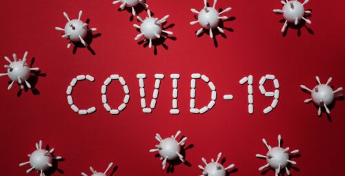 Covid-19 in white words on a red background with images of virus particles around it