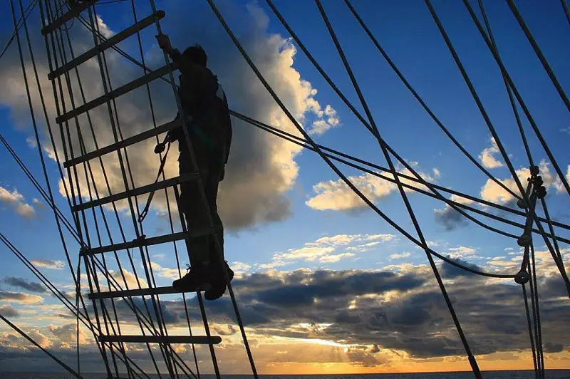 Image taken by blind photographer Roesie Percy of a man stanging on the ropes on a boat in the English Channel at sunset