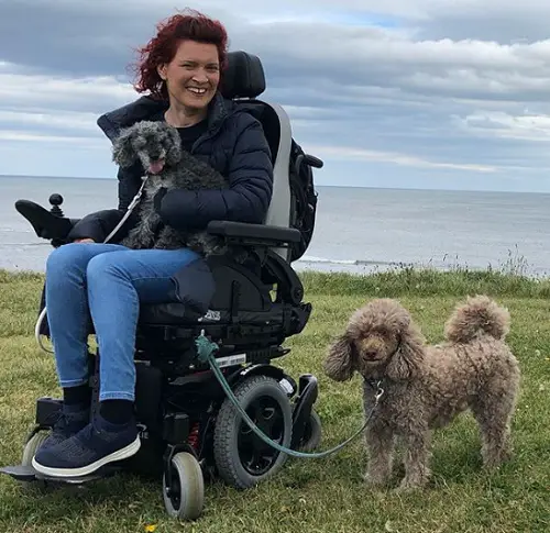 Lucy Reynolds in her wheelchair with her two dogs on a cliff top above the sea