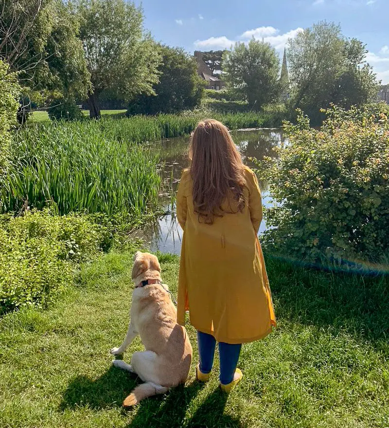 Emily standing on grass with dog looking at a lake