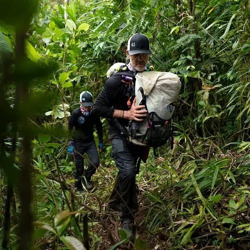 Hal Riley walking in a jungle carrying backpacks on his front and back