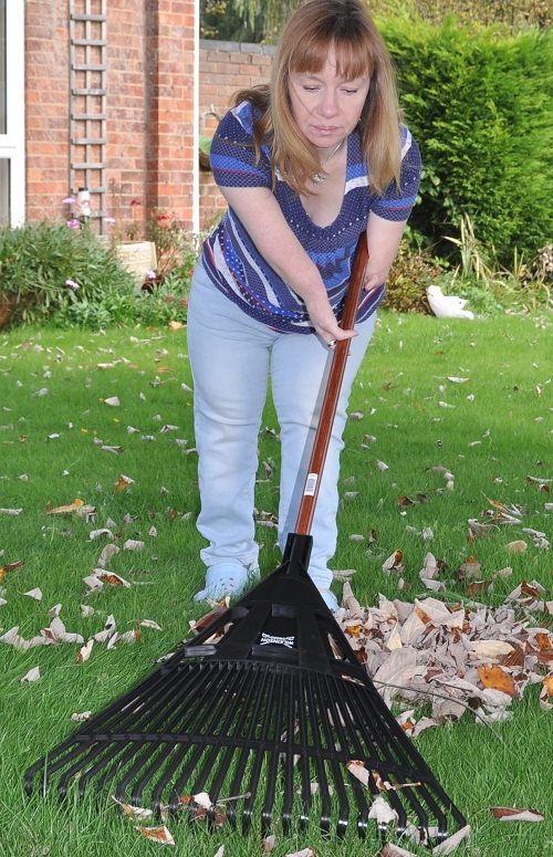 Disabled gardener Nikki Preston raking up leaves in her garden