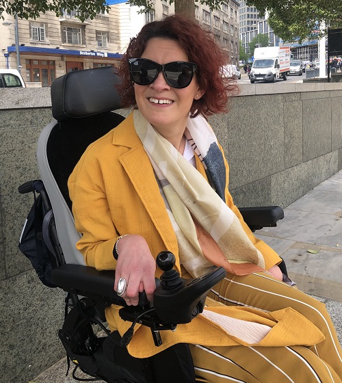 Dr Lucy Reynolds in a yellow jacket and skirt in her wheelchair on a pavement