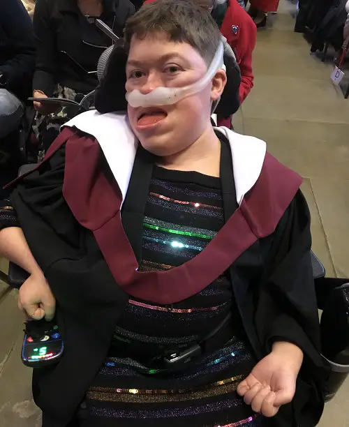 Stephanie in her wheelchair with her ventilator on wearing a black dress with coloured sequins