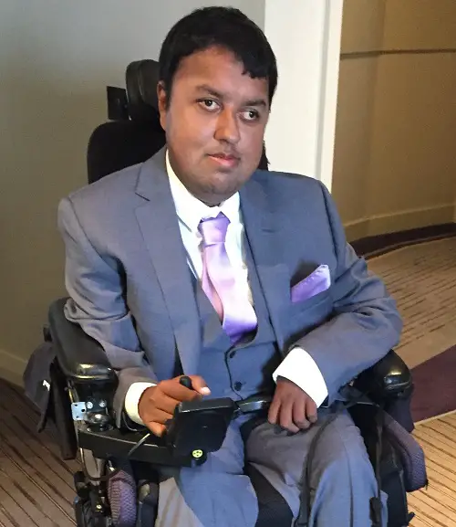 Nirav Shah in his wheelchair wearing a grey suit in a hotel room