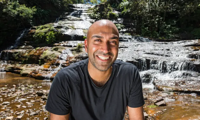 Blind presenter Amir Latif sitting on rocks in front of a waterfall