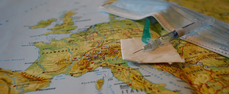 Covid-19 vaccine and face mask lying on a map of the world