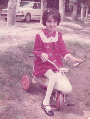 Disabled activist Raya AlJadir as a child wearing a red dress with white dots sat on a white bike