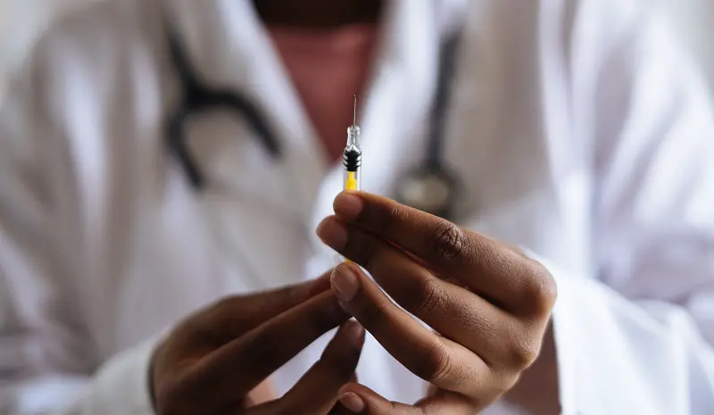 Syringe containing a vaccine being held by a doctor wearing a white coat