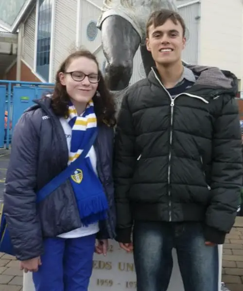 Sam and Ella at a football match outside the stadium both wearing dark puffer jackets and jeans
