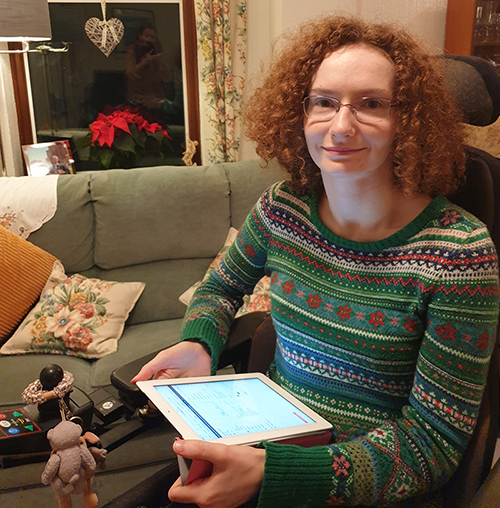 Hannah Deakin, smiling, wears a seasonal patterned winter jumper and holds her iPad