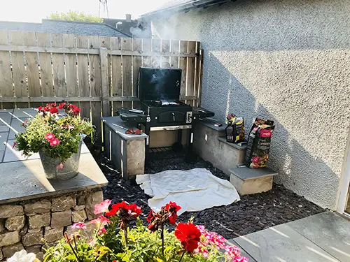 A barbeque sits in the corner of a beautiful garden
