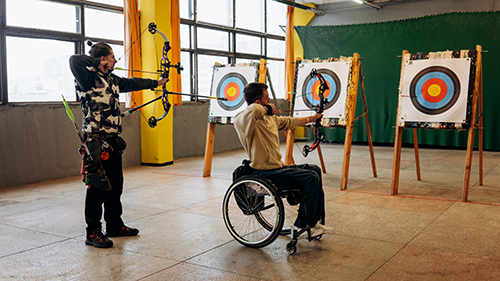 A lady and a man in a wheelchair are doing archery - Photo by Mikhail Nilov from Pexels