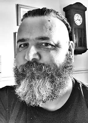 Black and white image of Zec who has a moustache and beard. He's wearing a round neck t-shirt 
