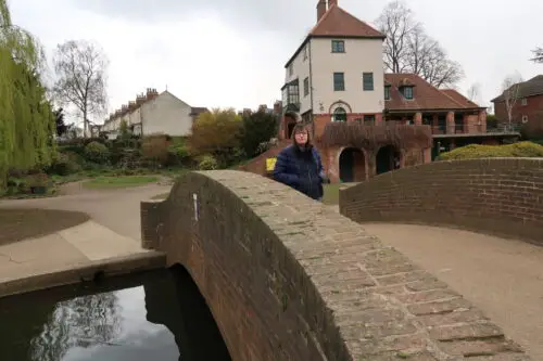 Holly-stood-on-a-stone-bridge-with-her-hands-in-her-pockets-she-is-wearing-a-blue-padded-jacket-and-blue-jeans-there-is-a-stone-building-in-the-background-