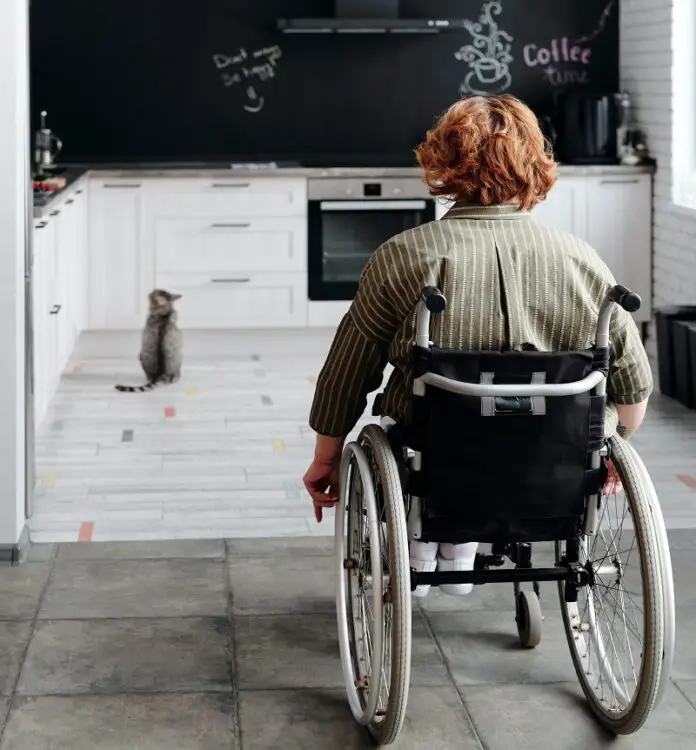 Woman in her wheelchair wheeling into her white kitchen from her open-plan dining room