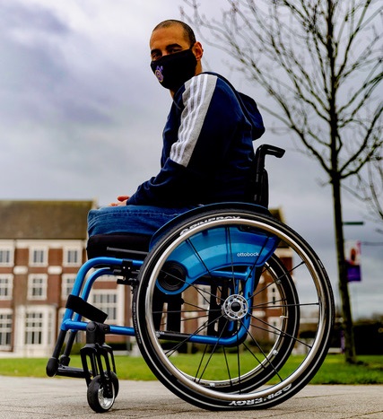 Paralympian Ali Jawad in his wheelchair outside wearing jeans, a blue hoodie and face mask