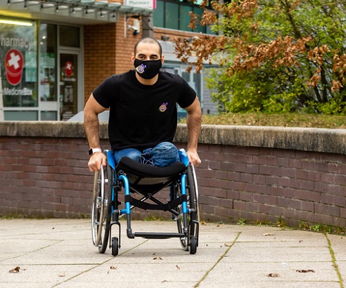 Paralympian Ali Jawad pushing his wheelchair wearing jeans, a black t-shirt and face mask