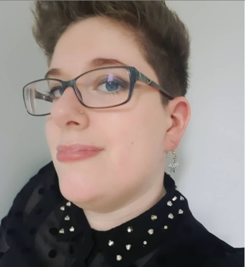Close up head shot of disabled blogger Dax with short spiky hair, black glasses and a black lace top
