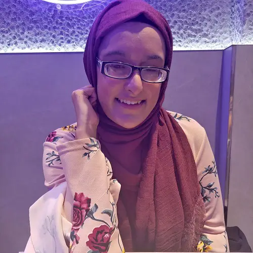 Nanjiba wearing glasses, a pink hijab and white top with pink flowers, sat in a restaurant