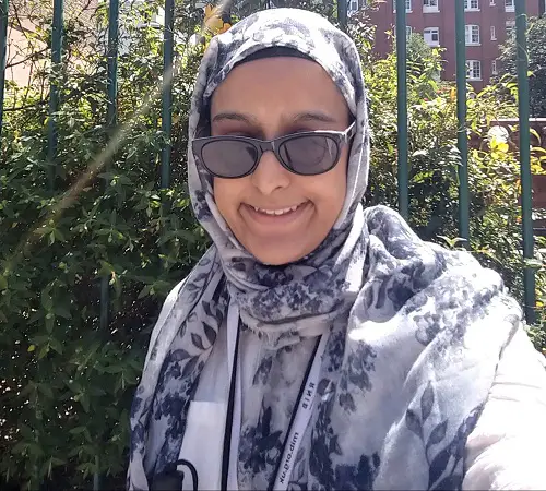 Nanjiba wearing glasses and a white hijab with blue flowers in a park in front of greenery