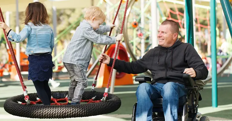 A man in a wheelchair with two children in a playground
