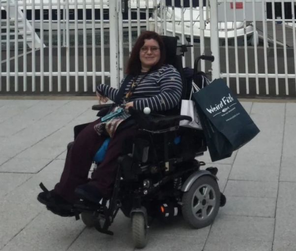 Emma Purcell in her powered wheelchair facing sidewards looking at the camera