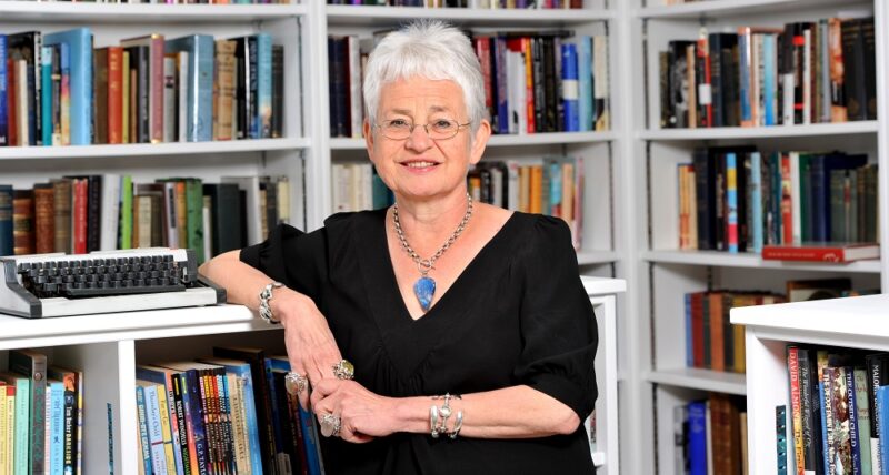 Jacqueline Wilson wearing a black top and glasses standing in front of white shelves filled with books - Imagine Children's Festival 2022 at Southbank Centre