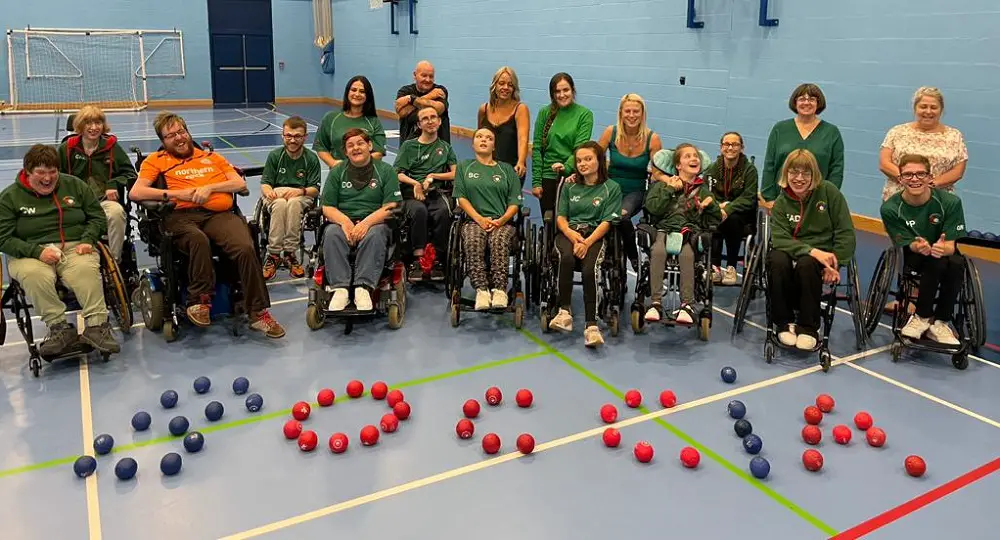 A group of disabled boccia players in a sports hall with the word boccia spelt out in balls in front of them