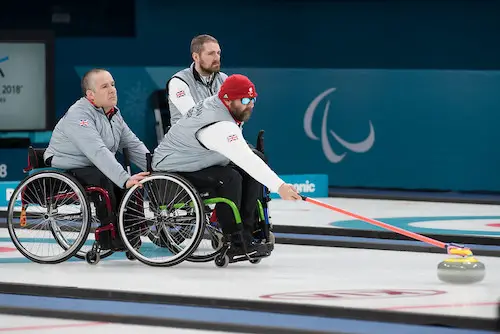 Wheelchair curler pushing curling stone with cue