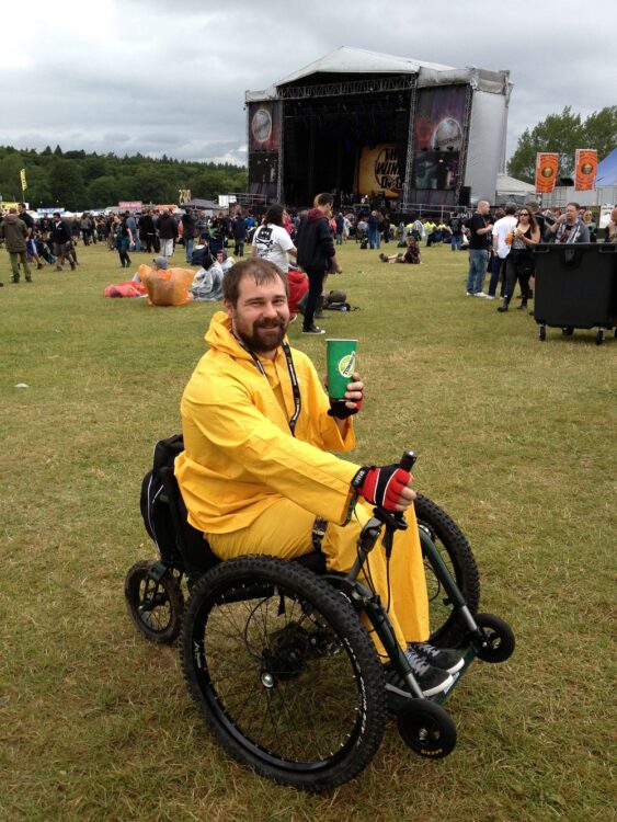 A man in a Mountain Trike all-terrian wheelchair and a raincoat at a festival