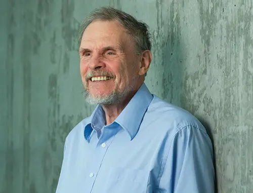 A close up of Geerat Vermeij wearing a light blue shirt with short grey hair and beard standing in front of a concrete wall